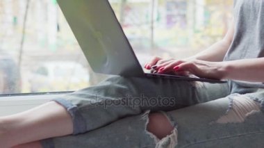 bir pencere pervazına üzerinde oturan ve bir dizüstü bilgisayar kullanarak bir kadın