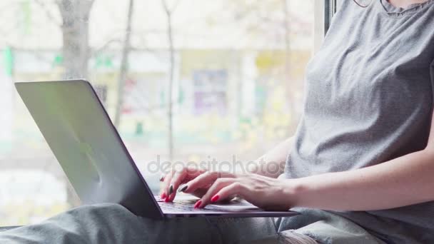 Jovem feliz sentada em uma soleira da janela e usando um laptop — Vídeo de Stock