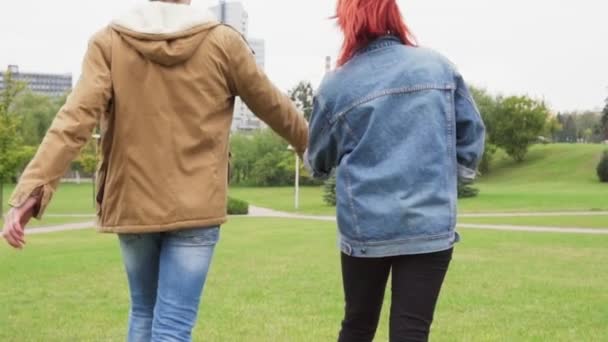 Молодая пара, держась за руки и гуляя в городском парке — стоковое видео