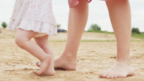 Menina com sua mãe caminha ao longo de uma praia de areia — Vídeo de Stock