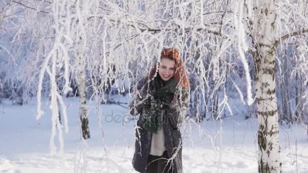 Lycklig ingefära kvinna knuffar en snötäckt gren och går till kameran — Stockvideo