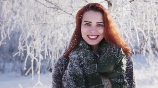 Chica pelirroja feliz sonriendo contra un árbol cubierto de nieve en un bosque de invierno — Vídeo de stock