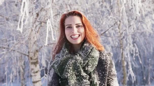 Молодая рыжая женщина смеется над заснеженным деревом в зимнем лесу — стоковое видео