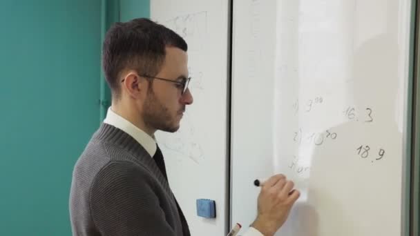 Γενειοφόρος άνδρας με γυαλιά που γράφει σε έναν πίνακα — Αρχείο Βίντεο