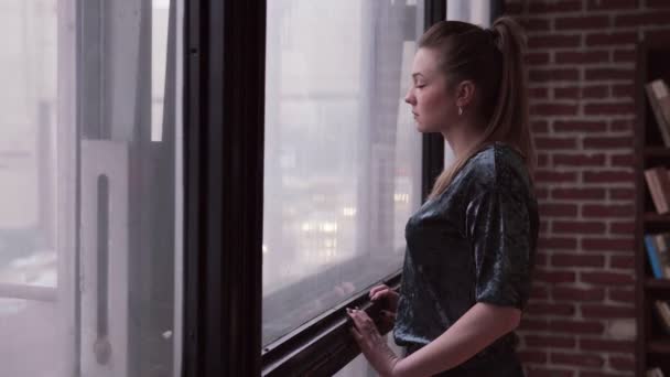 Сумна жінка дивиться на вулицю міста за вікном — стокове відео
