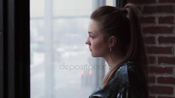 Ledsen flicka tittar ut genom fönstret och vänder huvudet — Stockvideo