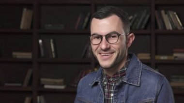 Gülümseyen, kitaplık arka plan gözlüklü genç erkek öğrenci