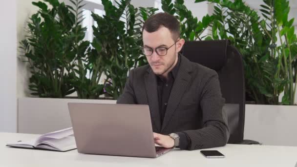 Vertrouwen zakenman met een bril met behulp van een laptop in kantoor — Stockvideo