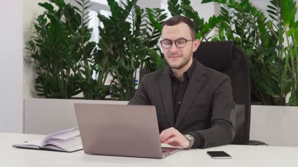 Успешный бизнесмен в костюме улыбается на рабочем месте в офисе — стоковое видео