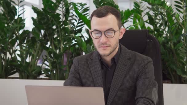 Joven hombre de negocios con gafas mira a la pantalla del ordenador portátil — Vídeo de stock