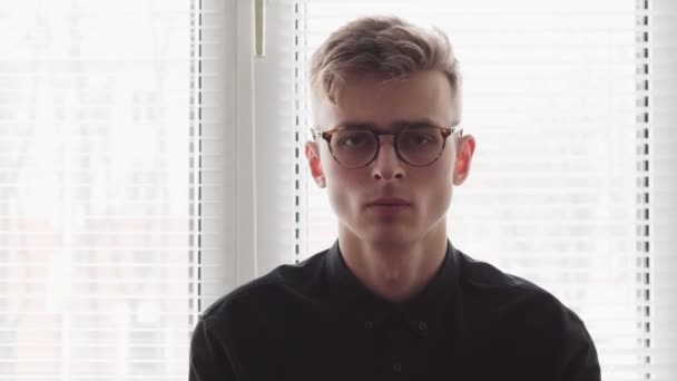 Лицо красивого молодого человека в очках у окна — стоковое видео