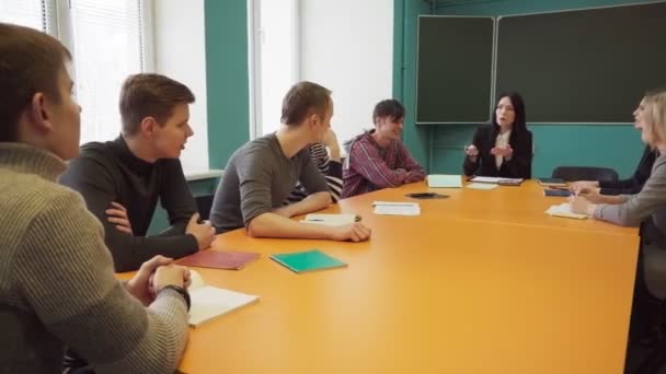 Groep studenten en een leraar zitten aan een tafel en praten — Stockvideo