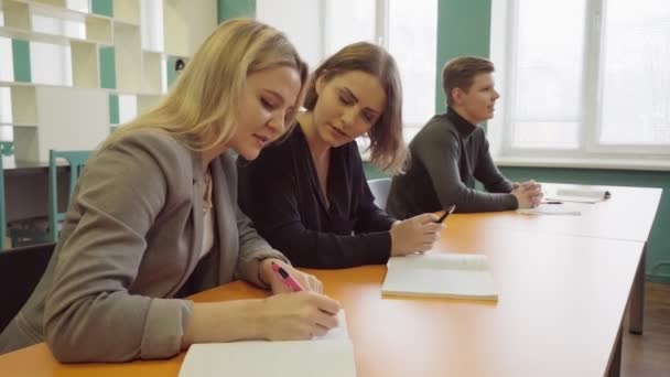 Kadın öğrenci bir not defterinde yazıyor ve onun arkadaşı için bir ders anlatıyor — Stok video