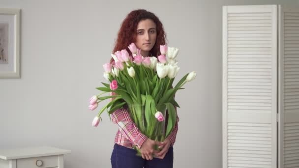 Νεαρή γυναίκα Μέσης Ανατολής με τα λυπημένα μάτια κρατώντας λουλούδια στα χέρια στο σπίτι — Αρχείο Βίντεο