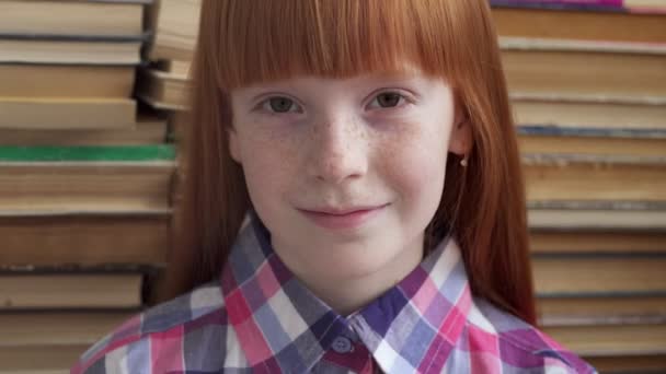 Крупним планом обличчя маленької щасливої школярки на тлі книг — стокове відео