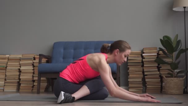 Joven mujer de fitness haciendo ejercicio de estiramiento en la estera en casa — Vídeo de stock