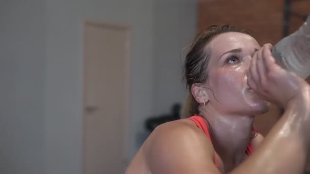 Cansada mujer fitness sudorosa bebe agua de una botella durante el entrenamiento en el gimnasio — Vídeos de Stock