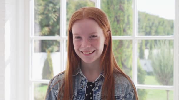 Happy ginger girl with freckles smiling against white window — Stock Video