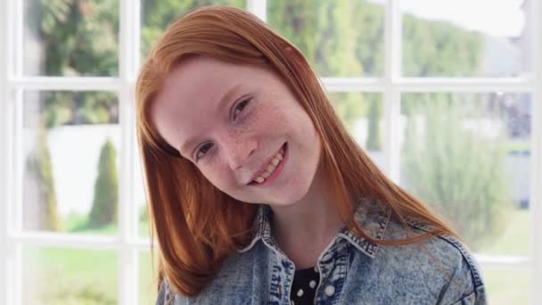 Αστείο πρόσωπο μιας έφηβης κοκκινομάλλας με φακίδες στο λευκό παράθυρο. — Αρχείο Βίντεο