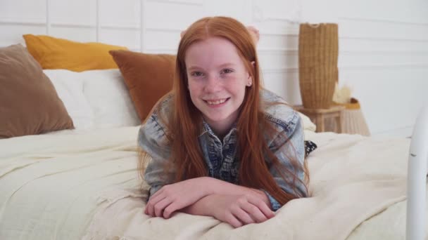 Гарненька дівчина-підліток з веснянками посміхається в спальні — стокове відео