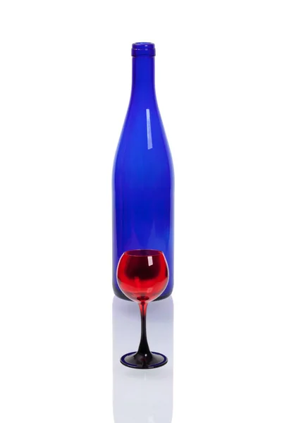 Láhev z modrého skla s červenou skleničku na bílé poza — Stock fotografie