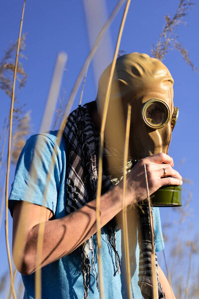 Man in gas mask holding his smoke mask. Guy in blue t shirt and scarf Shemagh in field. Environmental protection of ecology. Concept of infection, apocalypse and pollution. Hope concept. Anti virus.