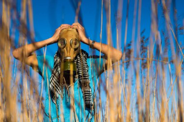 Gaz maskeli bir adam kafasını tutuyor. Mavi tişörtlü ve atkılı adam Shemagh sahada. Ekolojinin çevresel koruması. Enfeksiyon, kıyamet ve kirlilik kavramı. Umut kavramı. Anti virüs maskesi.
