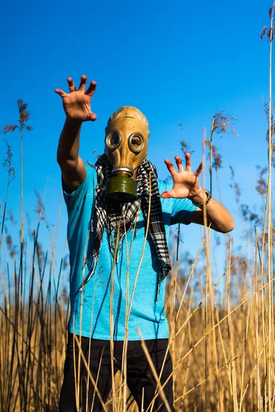 Man in gas mask crouching through the field with hand in blood. Guy in blue t shirt and scarf Shemagh. Concept of infection, apocalypse and pollution. Hope concept. Anti virus mask