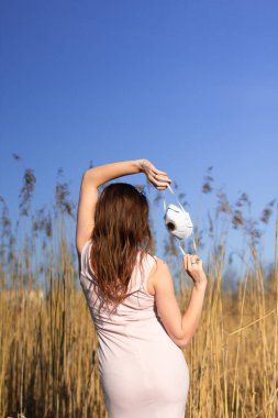 Olay yerinde elinde beyaz tıbbi maske tutan bir kız. Antivirüs ekipmanları. Pembe elbiseli zarif bir kadın. Pandemia 'nın sonu başarılı bir iyileşme. Umut kavramı, özgürlük, ters vuruş. Virüs koruması.  