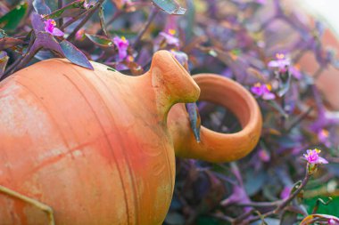 Bahçedeki menekşe çiçeği arka planına karşı çimlerin üzerinde antik kil esmer tencere. Peyzaj tasarımı. Bahçe malzemeleri, dekorasyon ve kırsal yaşam kavramı.    