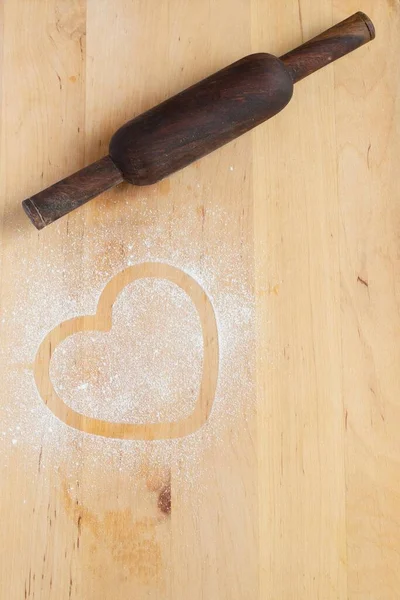 Heart prints and drawing with flour on the board with rolling pin. Rough wooden rectangular cutting board background with flour top view. Kitchen equipment Concept of baking copy space  hobby pastry