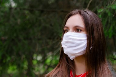 Yüzünde koruyucu tıbbi maske takan esmer genç bir kadın. Dışarıya yakından bakıyor. Yüz maskeli güzel bir esmer. Yeşil park. Uzayı kopyala Antivirüs, Enfeksiyon, Sağlık   