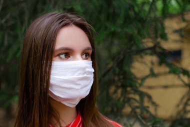 Yüzünde koruyucu tıbbi maske takan esmer genç bir kadın. Dışarıya yakından bakıyor. Yüz maskeli güzel bir esmer. Yeşil park. Uzayı kopyala Antivirüs, Enfeksiyon, Sağlık   