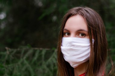 Yüzünde koruyucu tıbbi maske takan esmer bir kadın. Dışarıdaki kameraya yakından bakıyor. Yüz maskeli güzel bir esmer. Yeşil park. Uzayı kopyala Antivirüs, Enfeksiyon, Sağlık   