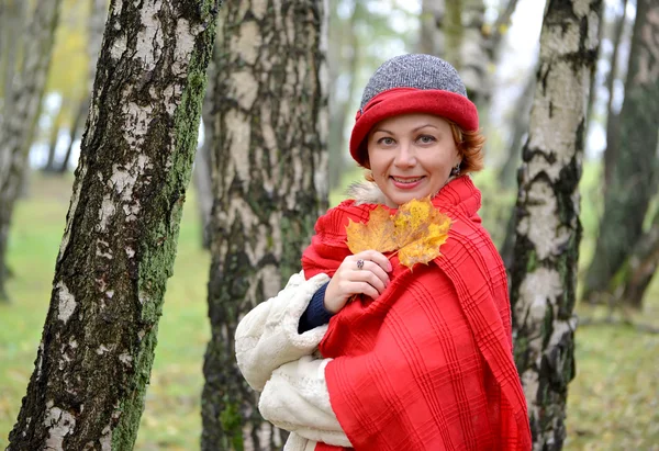 A mulher de anos médios em um chapéu e um vermelho roubou na madeira de vidoeiro — Fotografia de Stock