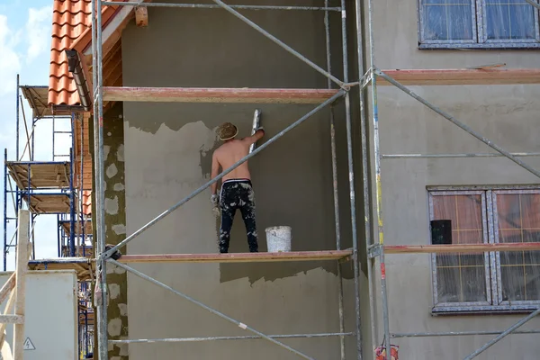 Kaliningrader Gebiet, Russland - 01. Juni 2016: Der Arbeiter putzt eine Hausfassade, die auf dem Bauholz steht — Stockfoto
