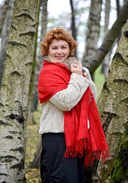 La femme joyeuse des années moyennes dans un étole rouge coûte parmi les bouleaux dans le bois — Photo