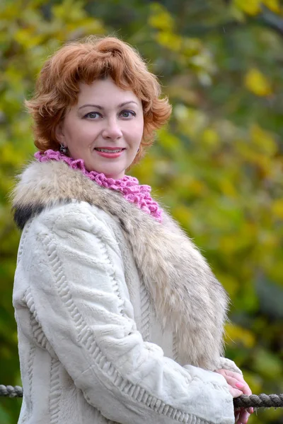 Portrait of the happy woman of average years against the background of autumn trees. Close up — Stock Photo, Image