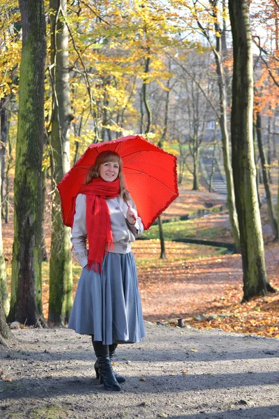 A jovem custa com um guarda-chuva vermelho no parque de outono — Fotografia de Stock