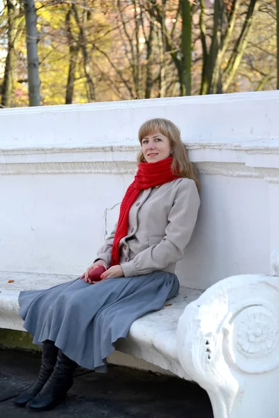 Молодая женщина с красным яблоком сидит на скамейке в осеннем парке — стоковое фото