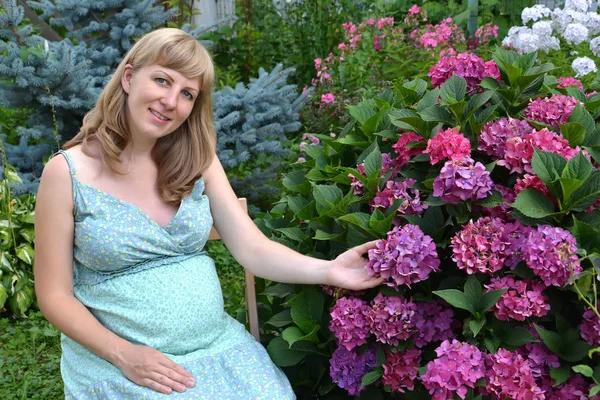 La jeune femme enceinte est assise dans un jardin près d'un buisson de l'hortensia florissante — Photo