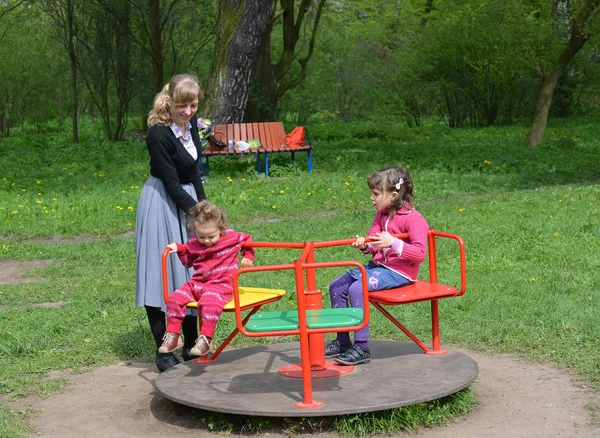 Die junge Frau überrollt zwei Kinder auf einem Kreisverkehr im Park — Stockfoto