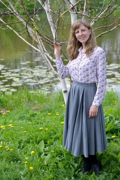 La joven se encuentra cerca del abedul floreciente de útil (Himalaya) (Betula utilis D.Don) en la orilla de un estanque — Foto de Stock