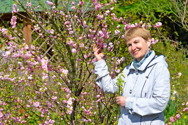 Zralá žena náklady mezi Kvetoucí keře mandle třílistá — Stock fotografie