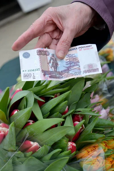 Пятьсот рублей в руке пожилой женщины на фоне тюльпанов — стоковое фото