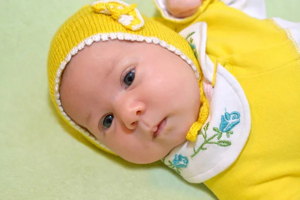 Портрет месячного ребенка в жёлтой кепке на зелёной спине — стоковое фото
