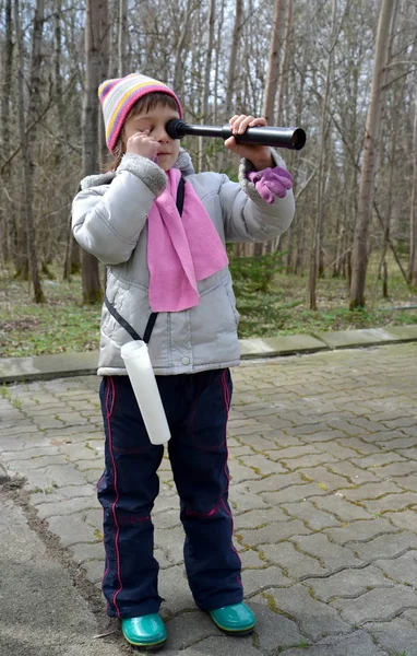 Holčička vypadá v dalekohledu, s zavřel jedno oko ruka — Stock fotografie