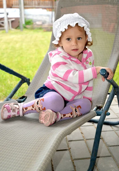 A menina senta-se em um salão de chaise no local do jardim — Fotografia de Stock