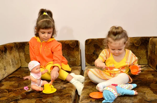 Dos hermanas pequeñas juegan con muñecas en un sofá — Foto de Stock