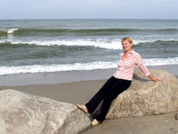 The woman of average years sits on a boulder. Coast of the Baltic Sea